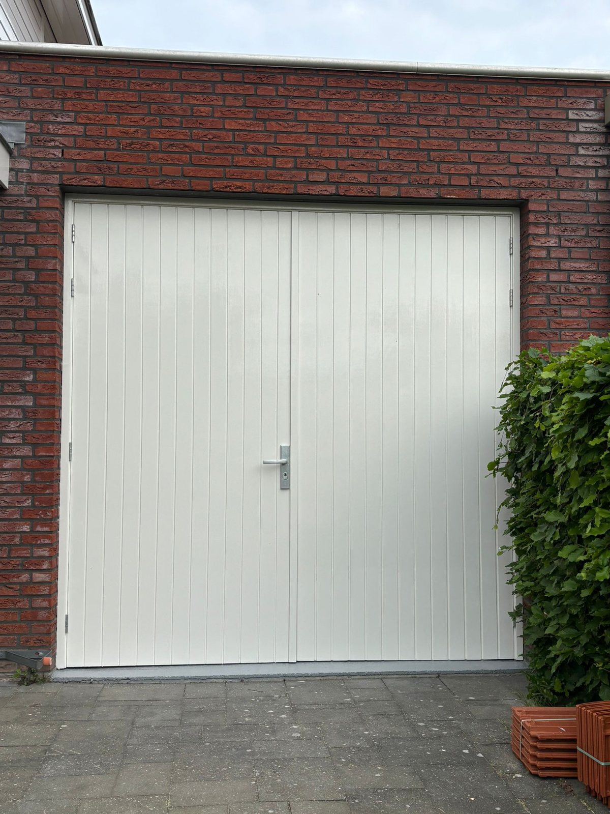 Crèmekleurige dubbele garagedeuren in een bakstenen muur