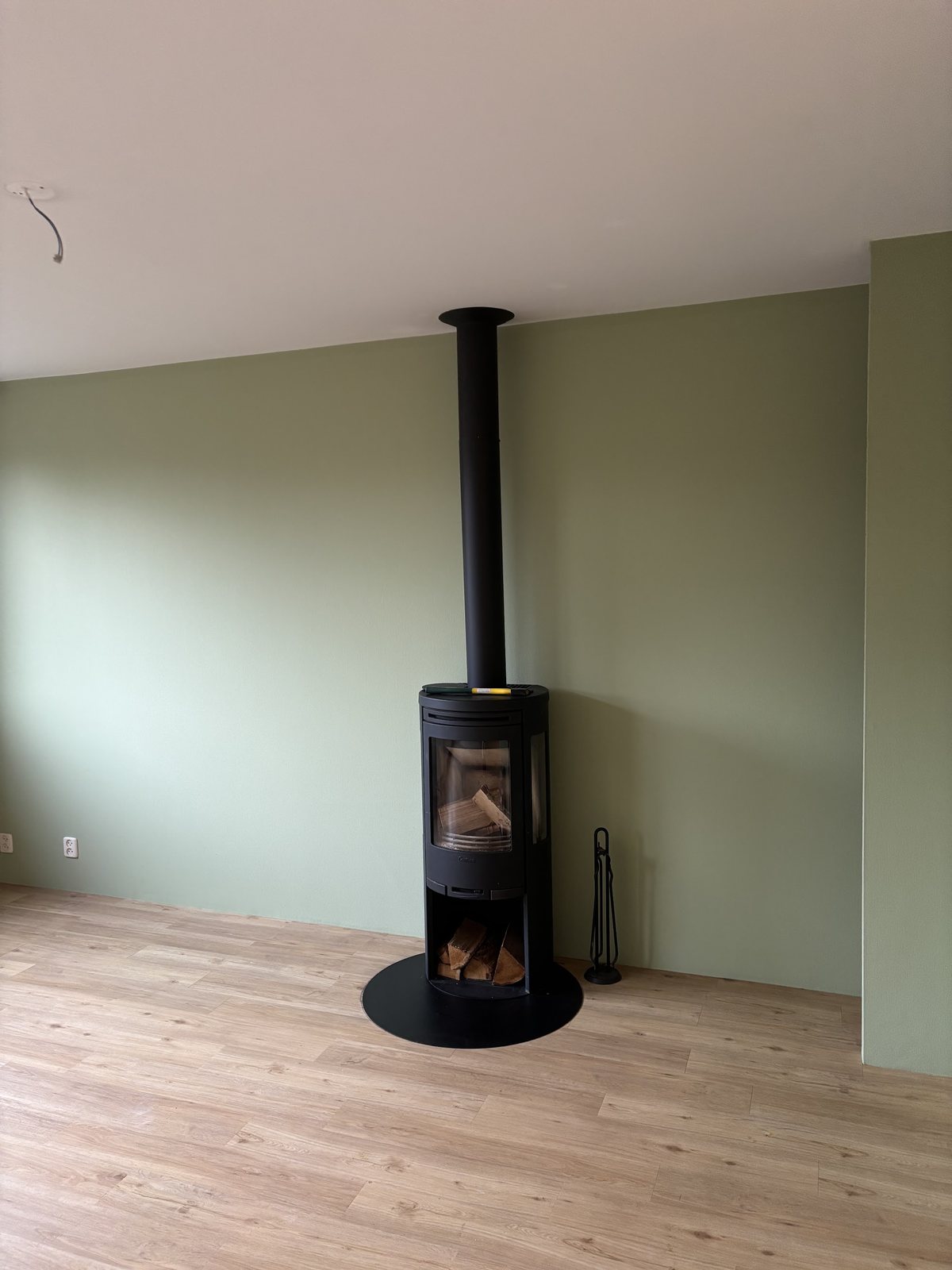 Saliegroene wand met een houtkachel en een nieuwe lichte vloer