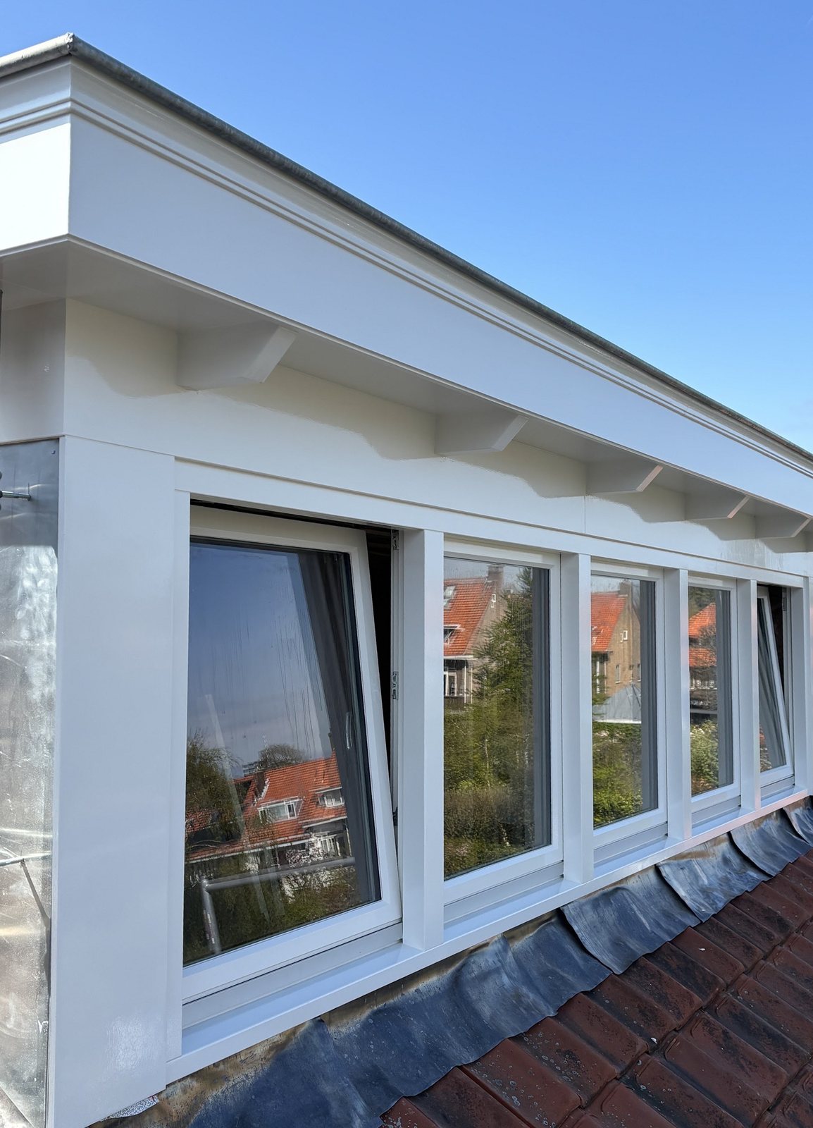 Wit geschilderde dakrand en kozijnen van een dakkapel tegen een blauwe lucht