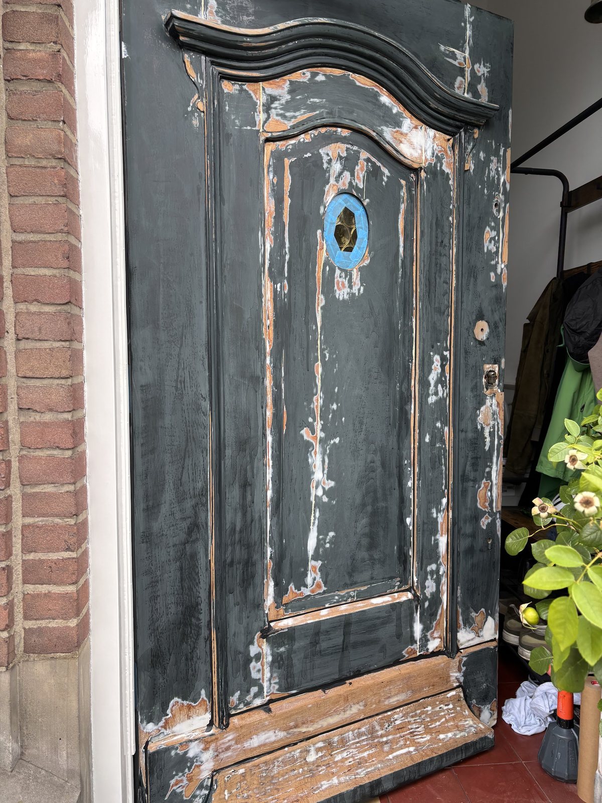 Voor: de voordeur kaal geschuurd tot op het hout, in een bakstenen kozijn