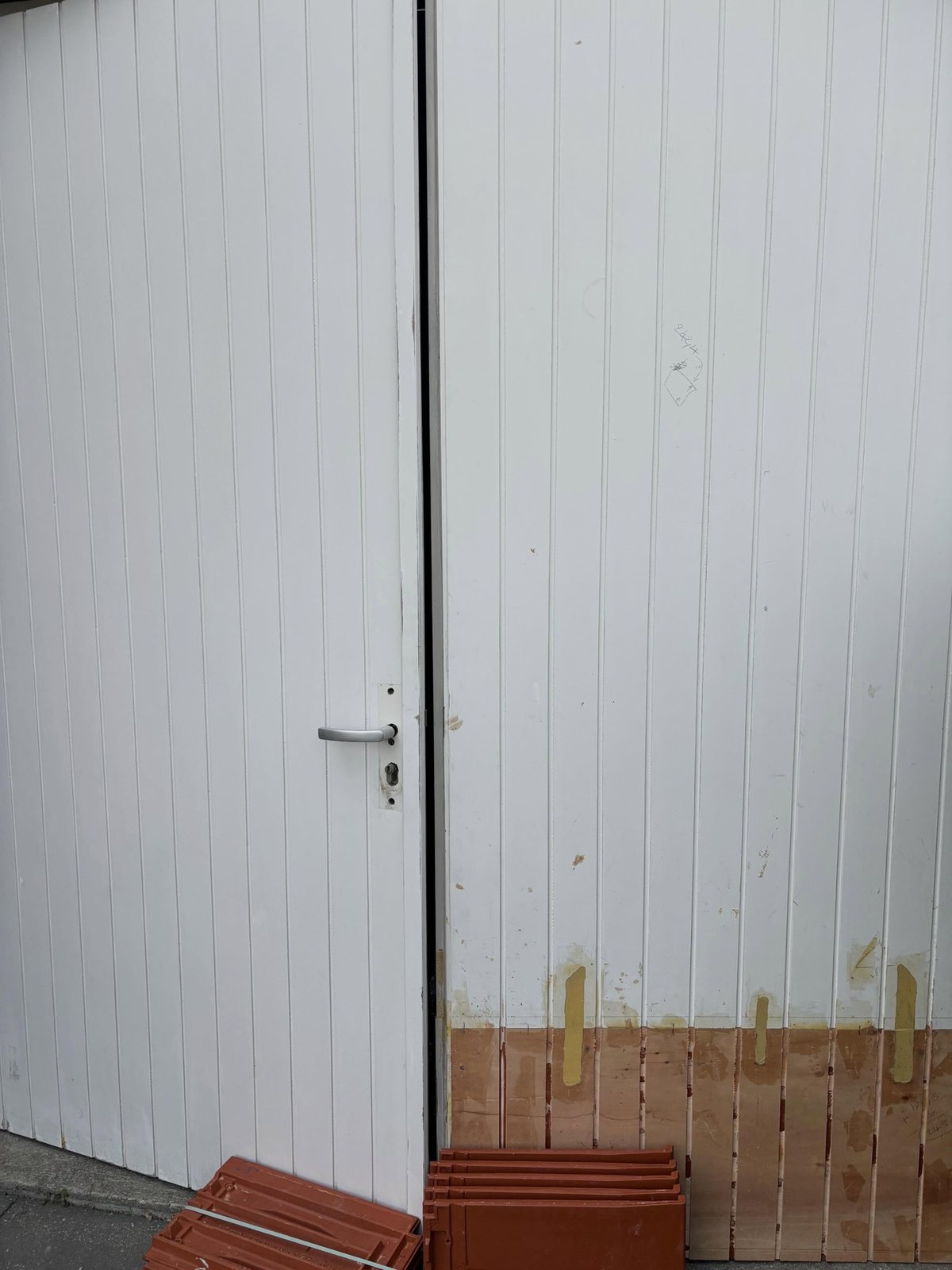 Witte garagedeuren met nieuw hout onderin, tijdens het herstel
